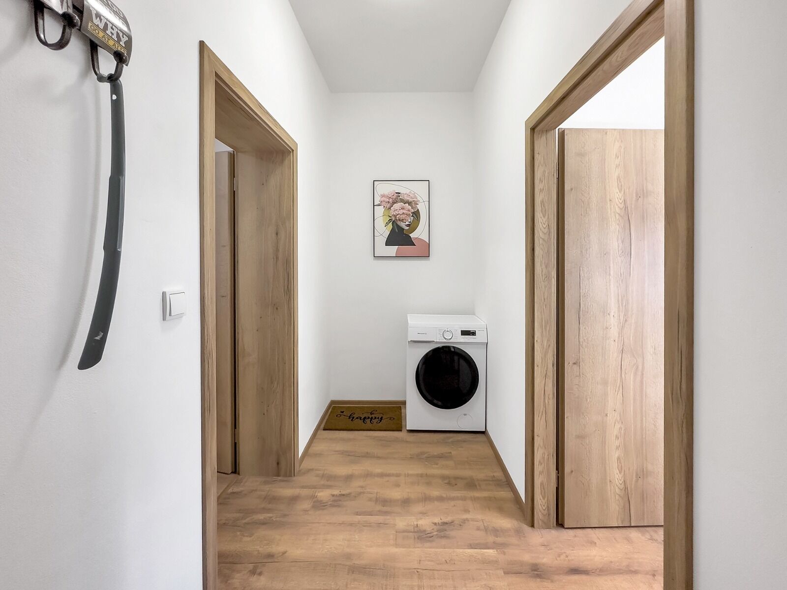 A narrow hallway with wooden doors, a washing machine, and a picture on the wall.
