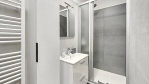Un baño moderno con cabina de ducha, lavamanos blanco y una toalla en el suelo.