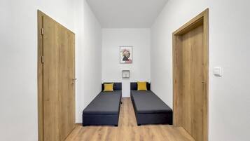 A room with two single beds, wooden doors, white walls, and a framed picture on the wall.