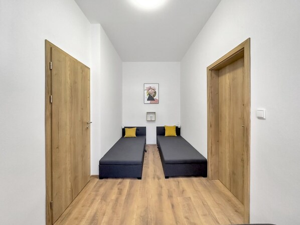 A room with two single beds, wooden doors, white walls, and a framed picture on the wall.