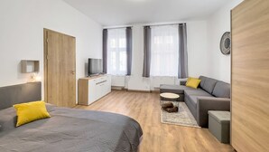 Una habitación moderna y bien iluminada con una cama, un sofá, una mesita y un televisor sobre un mueble de madera.