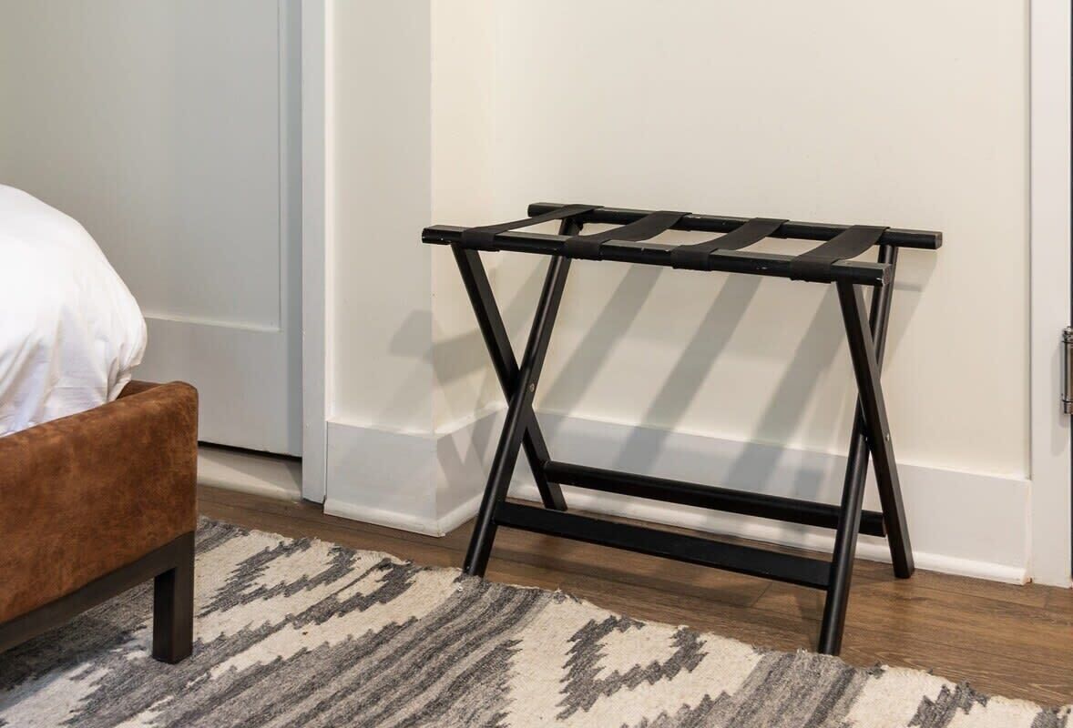 Ein Zimmer mit einem Bett, einem braunen Polsterstuhl, einem kleinen Nachttisch aus schwarzem Metall und einem gemusterten Teppich.