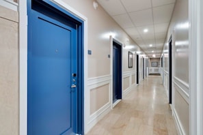 A long, narrow hallway with blue doors on the left and white doors on the right.