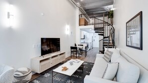 A modern living room with a sofa, coffee table, and TV. There is a staircase leading to an upper level.