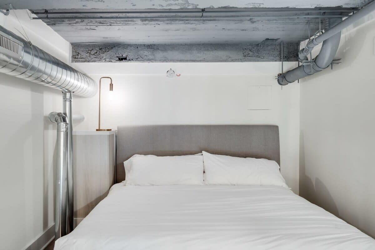 Une chambre d’hôtel minimaliste, comprenant un lit, une table de chevet et une lampe moderne.