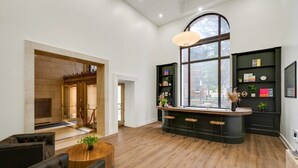 A spacious living area with a wooden floor, a central bar with stools, a large window, and a fireplace.
