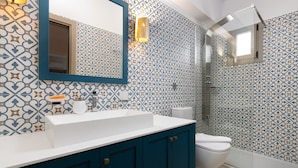 Een badkamer met patroon tegels, een witte wastafel, een blauwe kast, een toilet en een douche met een glazen deur.