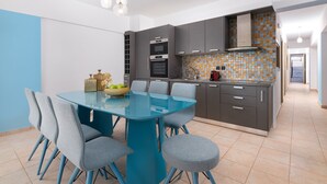 Een moderne keuken met een blauwe eettafel, grijze stoelen en een betegelde spatwand.