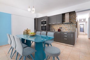 A modern kitchen with a blue dining table, grey chairs, and a tiled backsplash.