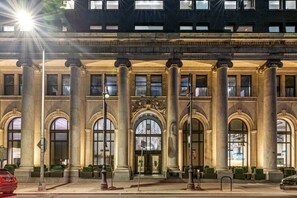 Un imposant bâtiment doté de grandes colonnes et de fenêtres en arc de cercle, sur lequel on peut lire l’inscription « JOURNAL PUBLIC ».