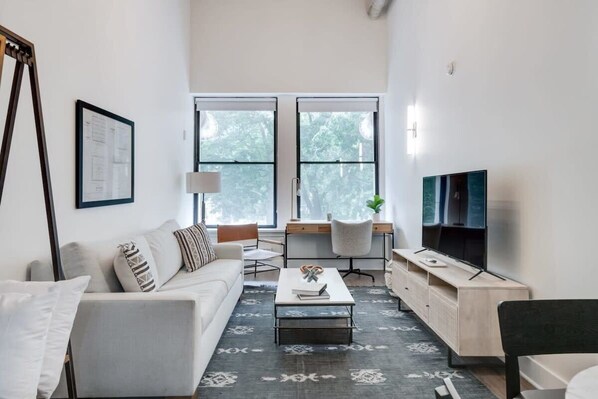 Un salon moderne comprenant un canapé, une table basse, un téléviseur et un bureau avec une chaise.
