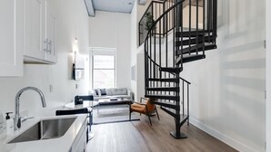 A modern kitchen with a built-in sink and a staircase with black railings leading to an upper level. - Sosuite | 2BR Loft w W/D, Gym, Lounge (Philadelphia)