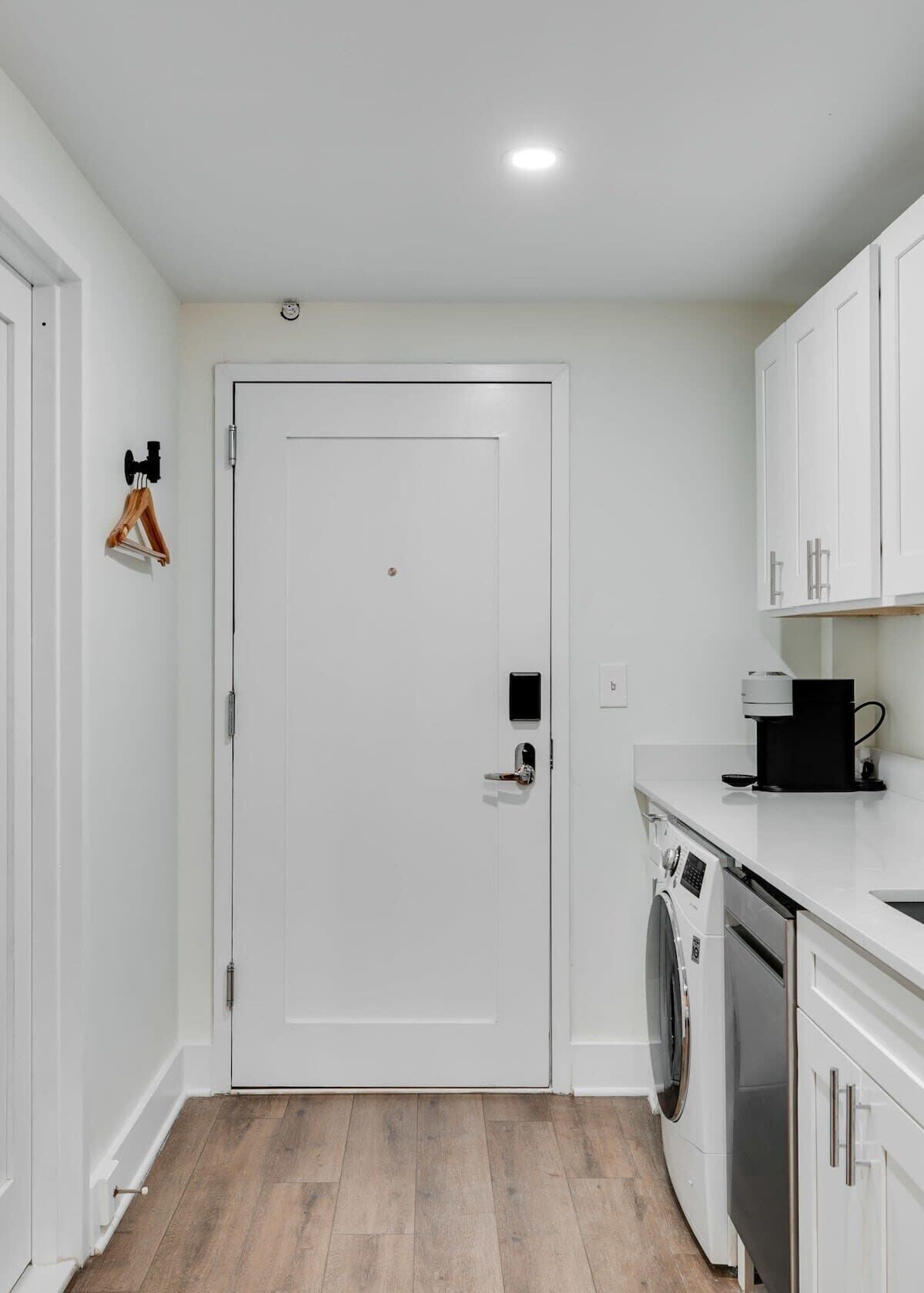 A compact kitchen with a washing machine, a coffee maker, and a door with a security lock.