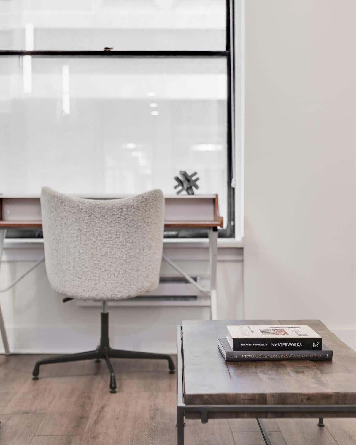 A modern office chair with a textured seat, a small table with books, and a window with blinds.