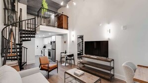 A spacious living area with a modern staircase, a flat-screen TV, and a dining area. - Sosuite | 1BR Loft w W/D, Gym, Lounge (Philadelphia)