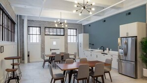 A modern kitchen with a dining area, featuring a large wooden table, multiple chairs, a stainless steel refrigerator, and a hanging light fixture. - Sosuite | 1BR Loft w W/D, Gym, Lounge (Philadelphia)
