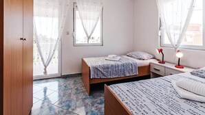 Une chambre avec deux lits, une armoire en bois, une fenêtre avec des rideaux légers et un sol carrelé.