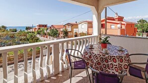 Un balcon avec une table et des chaises, donnant sur une ville côtière avec ses bâtiments et un ciel dégagé.