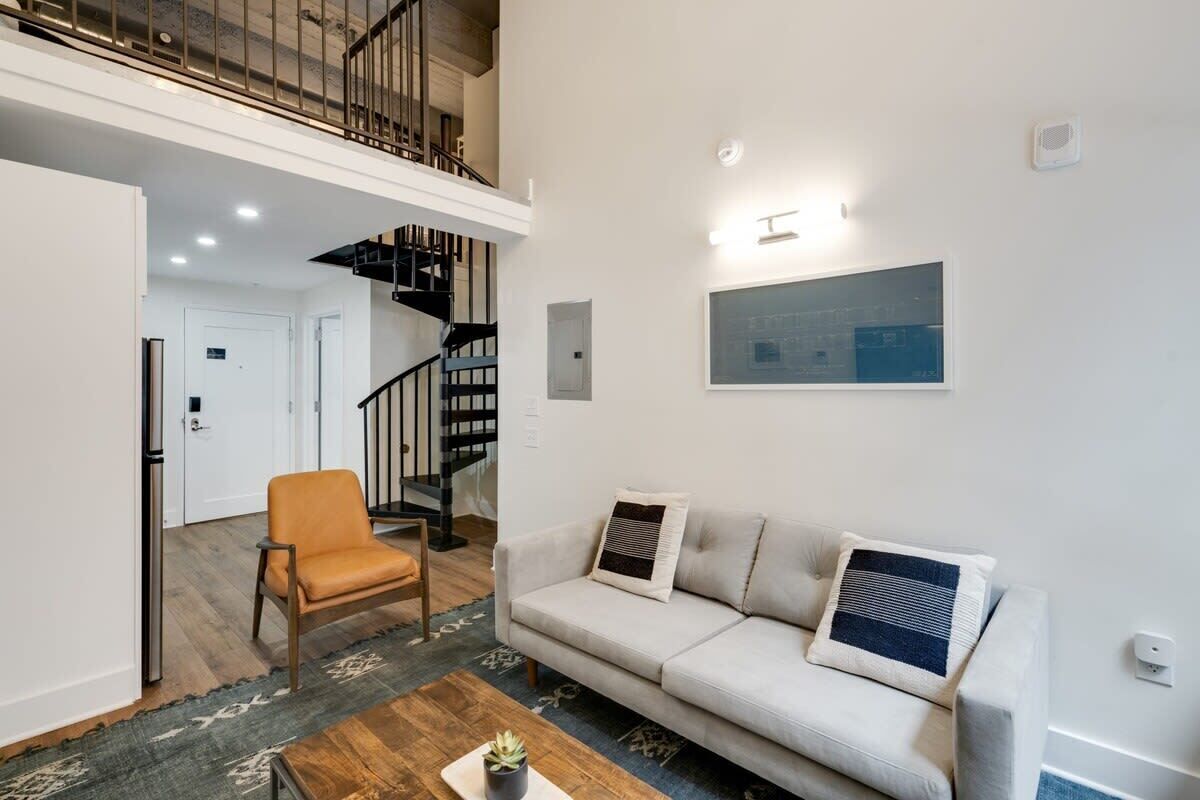 A spacious living area with a high ceiling, a staircase, a sofa, a chair, and a coffee table.