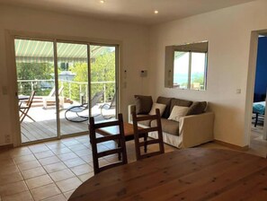 Une pièce dotée d’une porte-fenêtre coulissante donnant sur une terrasse, d’un canapé, d’une chaise en bois et d’une petite table.