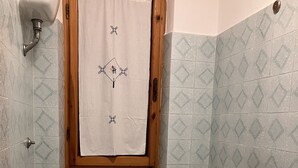 Un bagno con il water, un bidet e due lavandini. Un asciugamano è appeso a una finestra con cornice in legno, un cesto è posizionato su un mobile e un porta carta igienica è montato sulla parete.