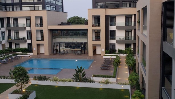 Ein modernes Gebäude mit einem zentralen Innenhof, der einen Swimmingpool, Lounge-Bereiche und Grünflächen umfasst.