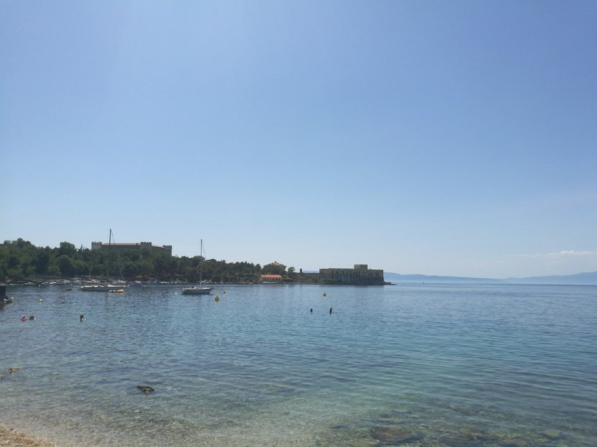 A coastal scene with clear water, boats, and buildings along the shore.