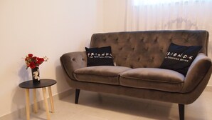 Ein braunes Sofa mit zwei schwarzen Kissen, ein kleiner schwarzer Tisch mit Blumenvase und eine schlichte weiße Wand.