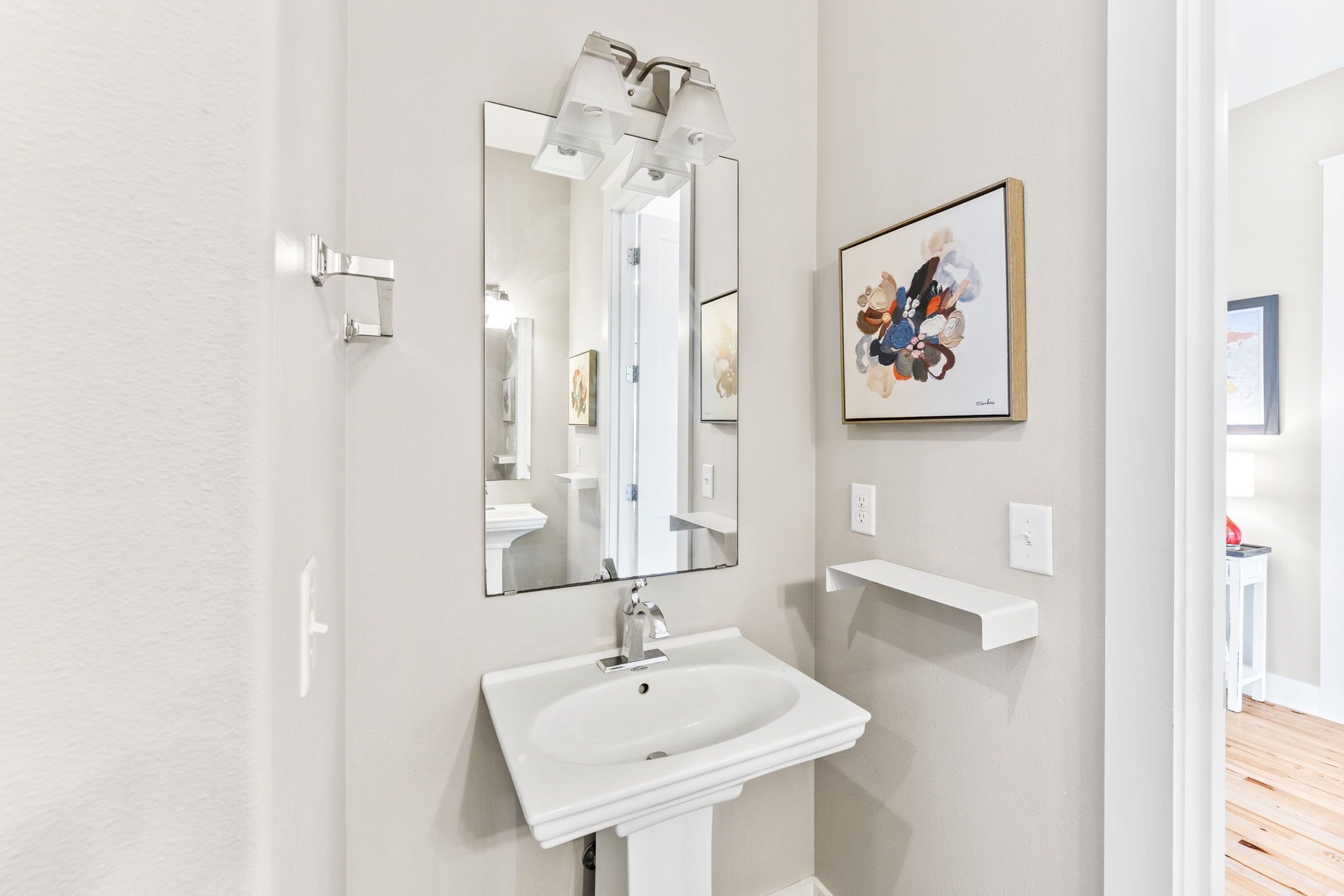 A bathroom with a white sink, a large mirror, and a framed artwork on the wall.