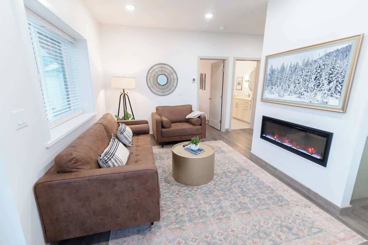 A living room with a brown sofa, a round coffee table, a fireplace, and a winter-themed painting.