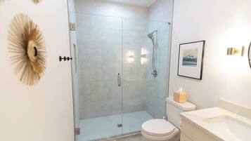 A modern bathroom with a glass-enclosed shower, a toilet, and a sink.