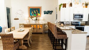 Een moderne keuken met witte kastjes, een granieten aanrechtblad en een eethoek met rieten stoelen en een houten tafel.