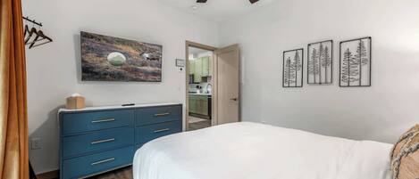 A bedroom with a bed, a dresser, a ceiling fan, and artwork on the walls.