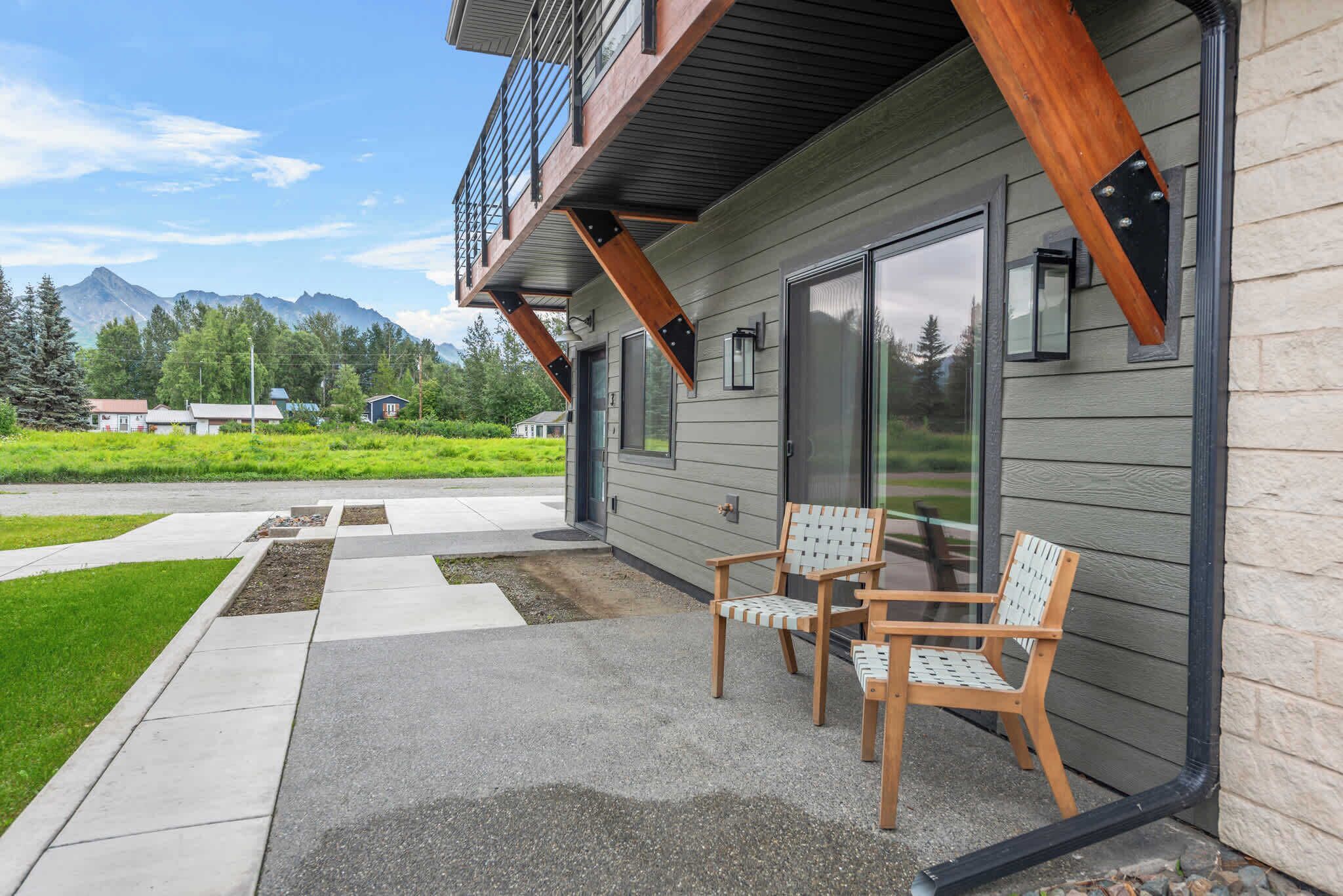 A modern building with a balcony, two wooden chairs, and a view of mountains.