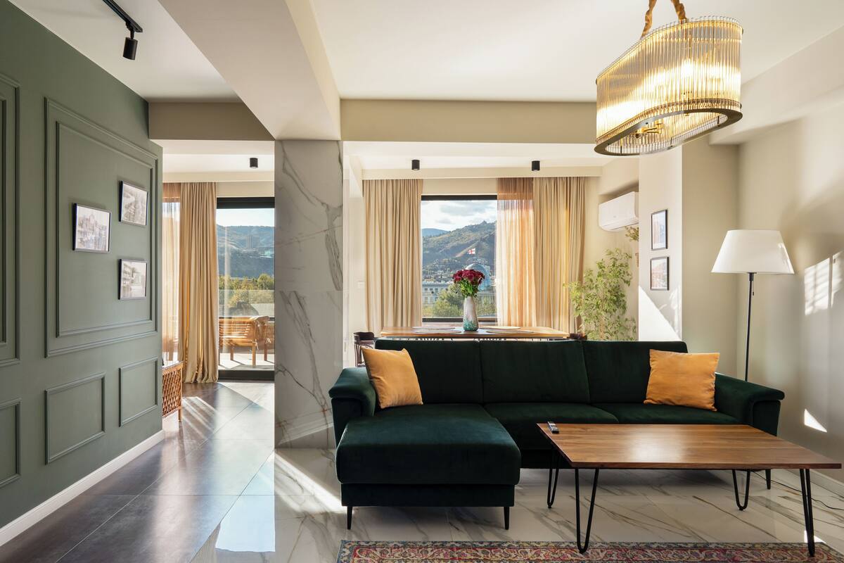 Een moderne woonkamer met een donkergroene modulaire bank, een houten salontafel en een kroonluchter.
