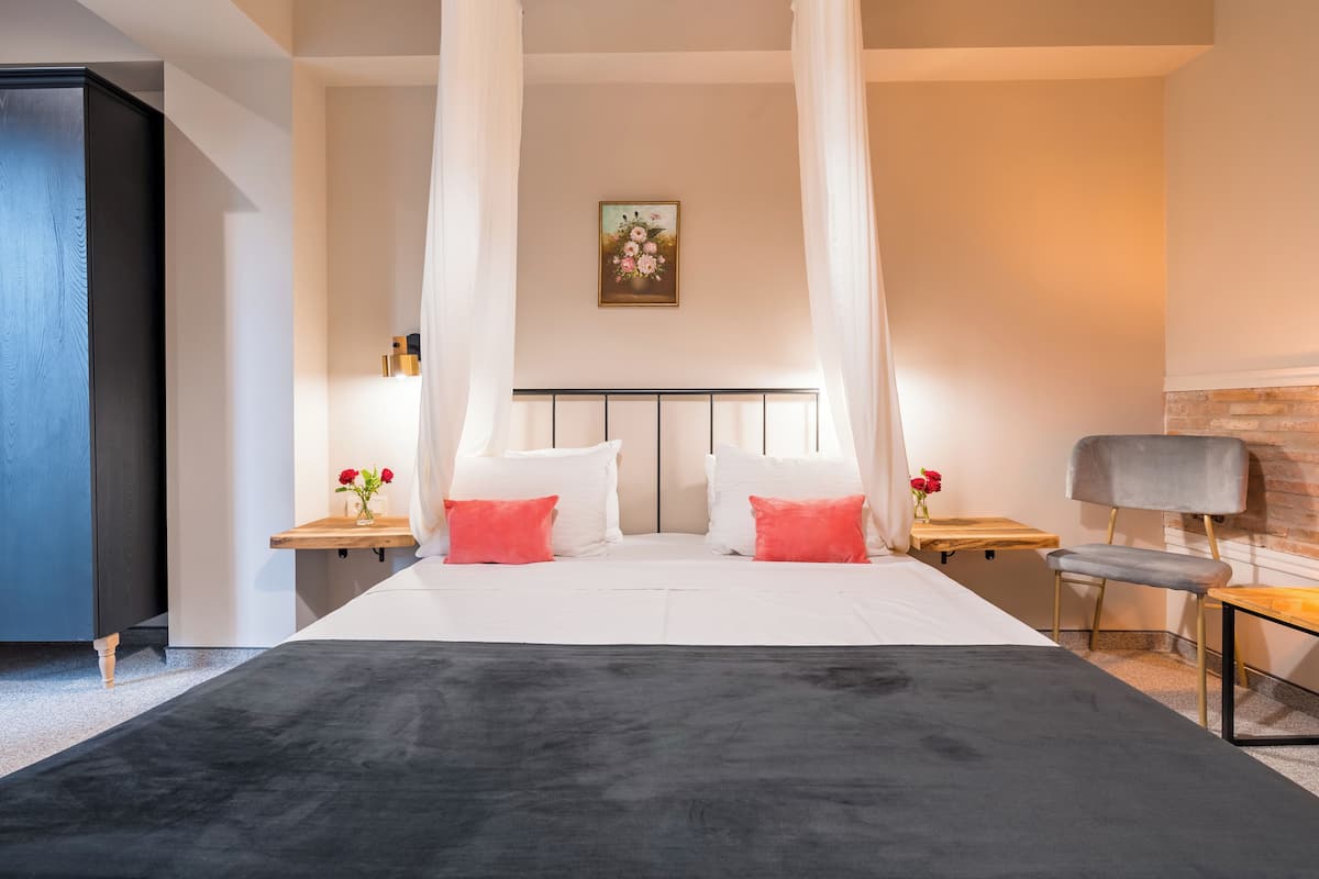 Een slaapkamer met een bed, nachtkastje, stoel en een schilderij aan de muur.