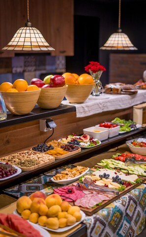 Un bufé con diferentes opciones de comida, incluyendo frutas, quesos y embutidos.