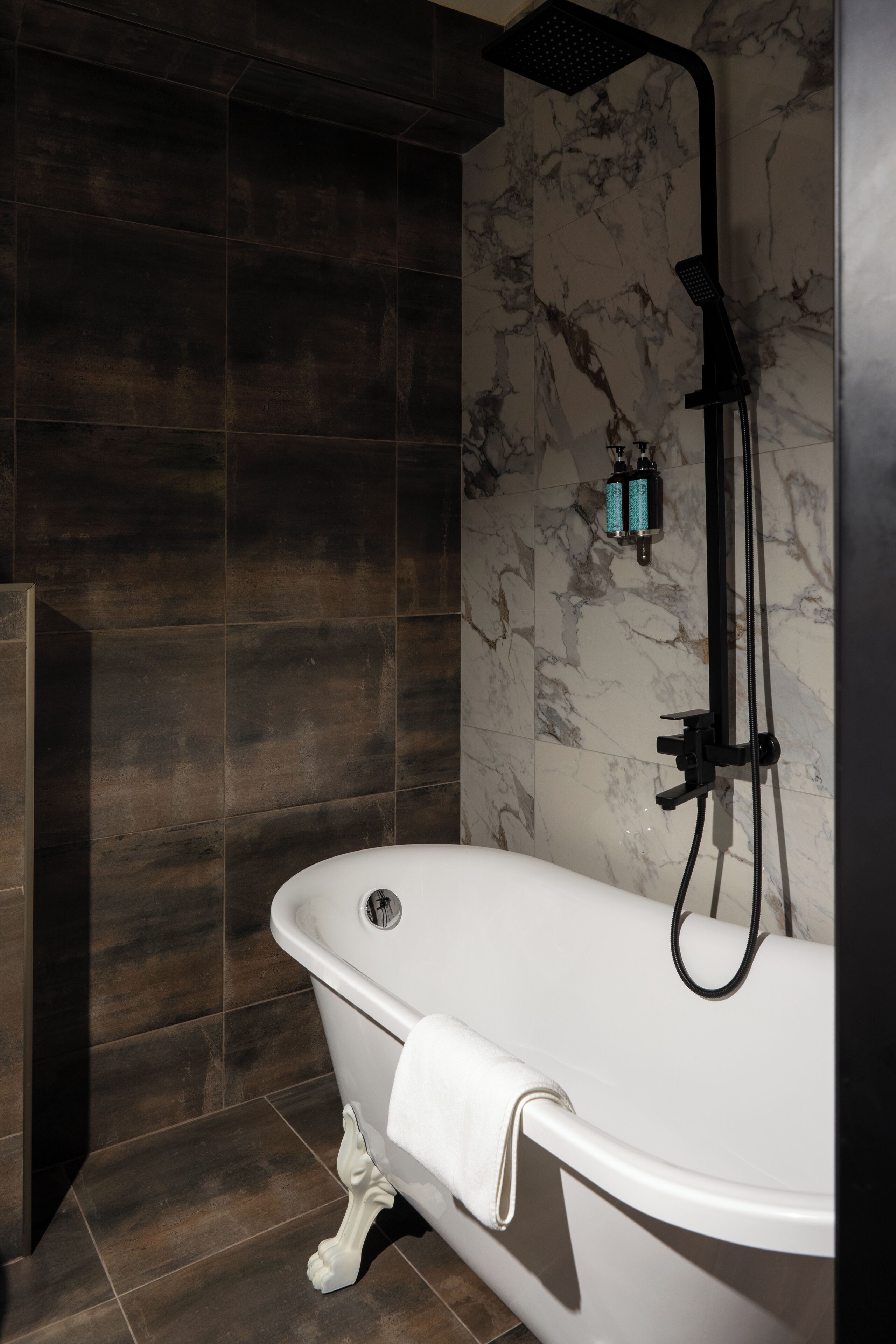 Un baño moderno con una bañera independiente, un cabezal de ducha y azulejos de mármol en las paredes.