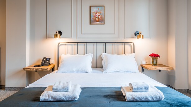 A hotel room with a large bed, two bedside tables, a wall-mounted painting, and a vase with flowers.