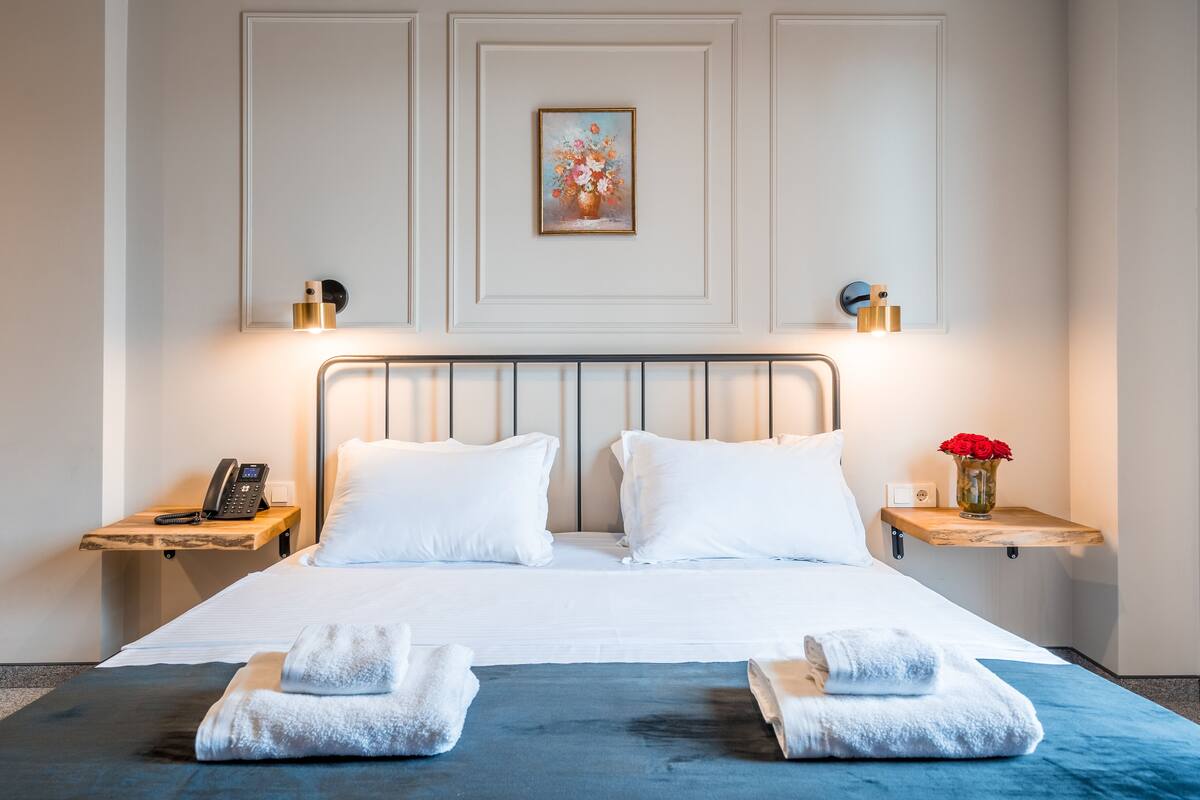 Een hotelkamer met een groot bed, twee nachtkastjes, een aan de muur hangend schilderij en een vaas met bloemen.