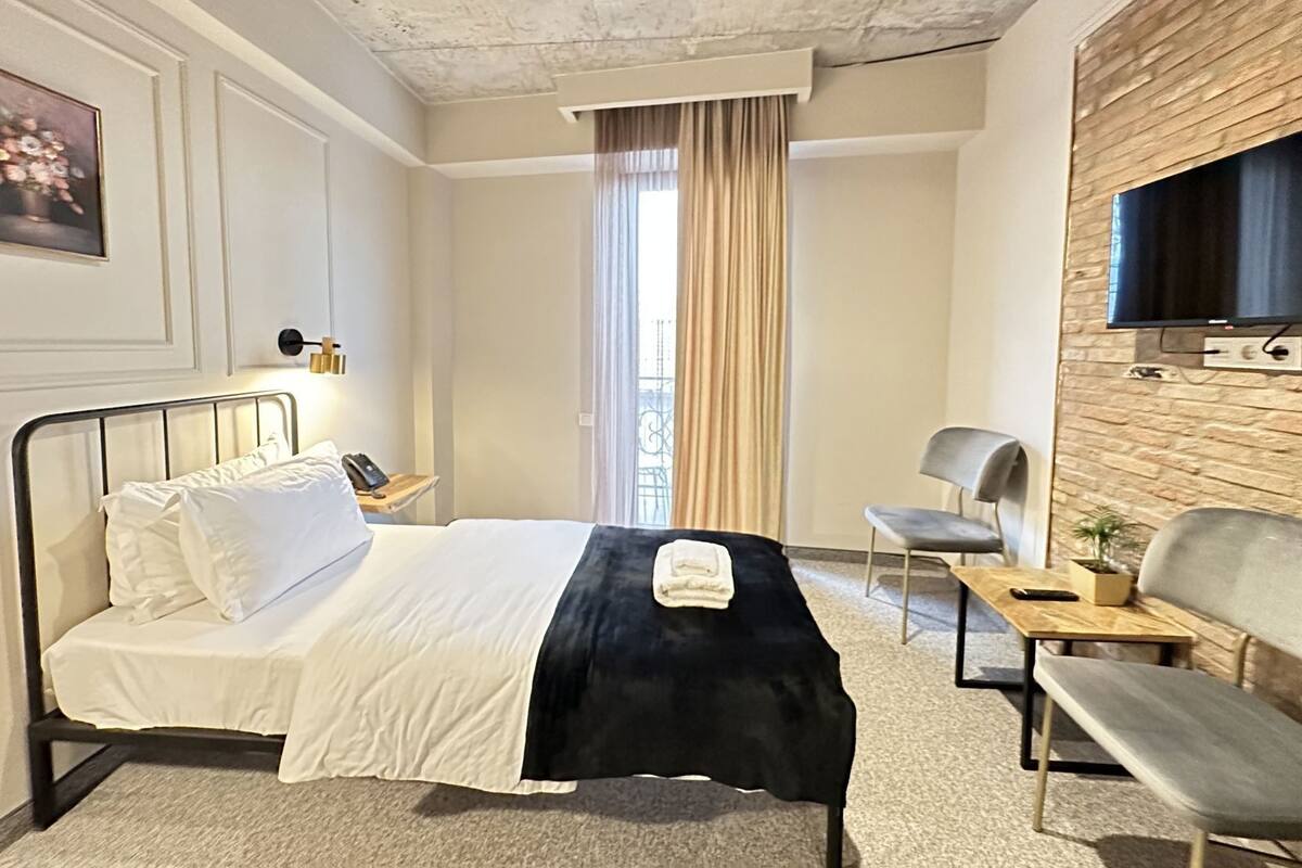 Een hotelkamer met een bed, een bureau, een stoel, een televisie en een raam met gordijnen.