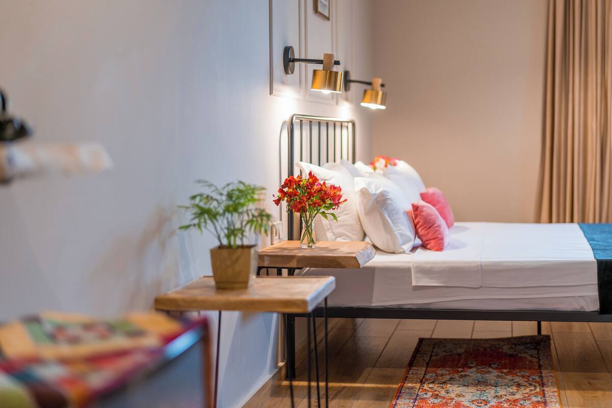 Een kleine slaapkamer met een bed, nachtkastje en een potplant.