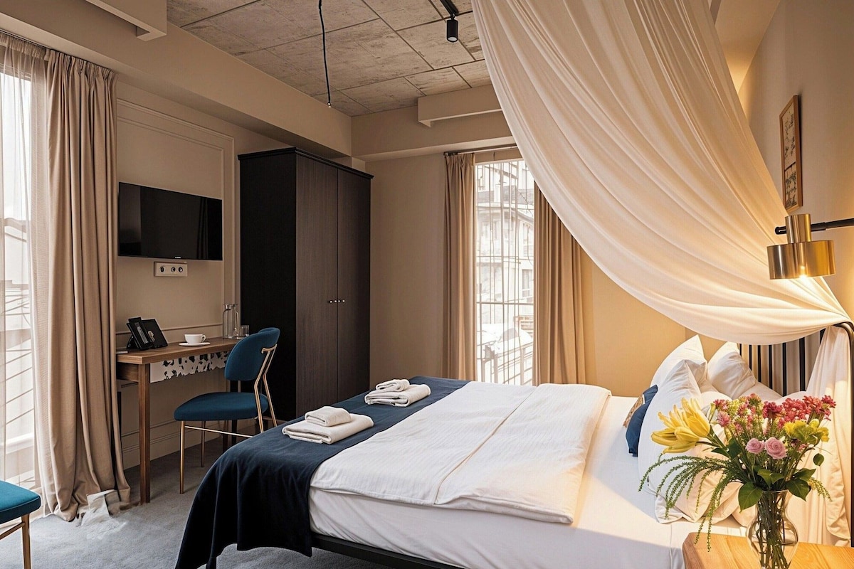 A hotel room with a bed, a desk, a TV, and a window with curtains.