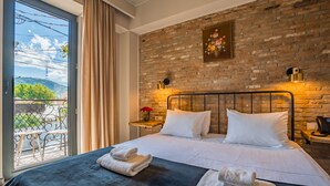 Ett hotellrum med en tegelvägg, en stor säng med vita sängkläder, en balkong med utsikt och en tavla ovanför sängen.