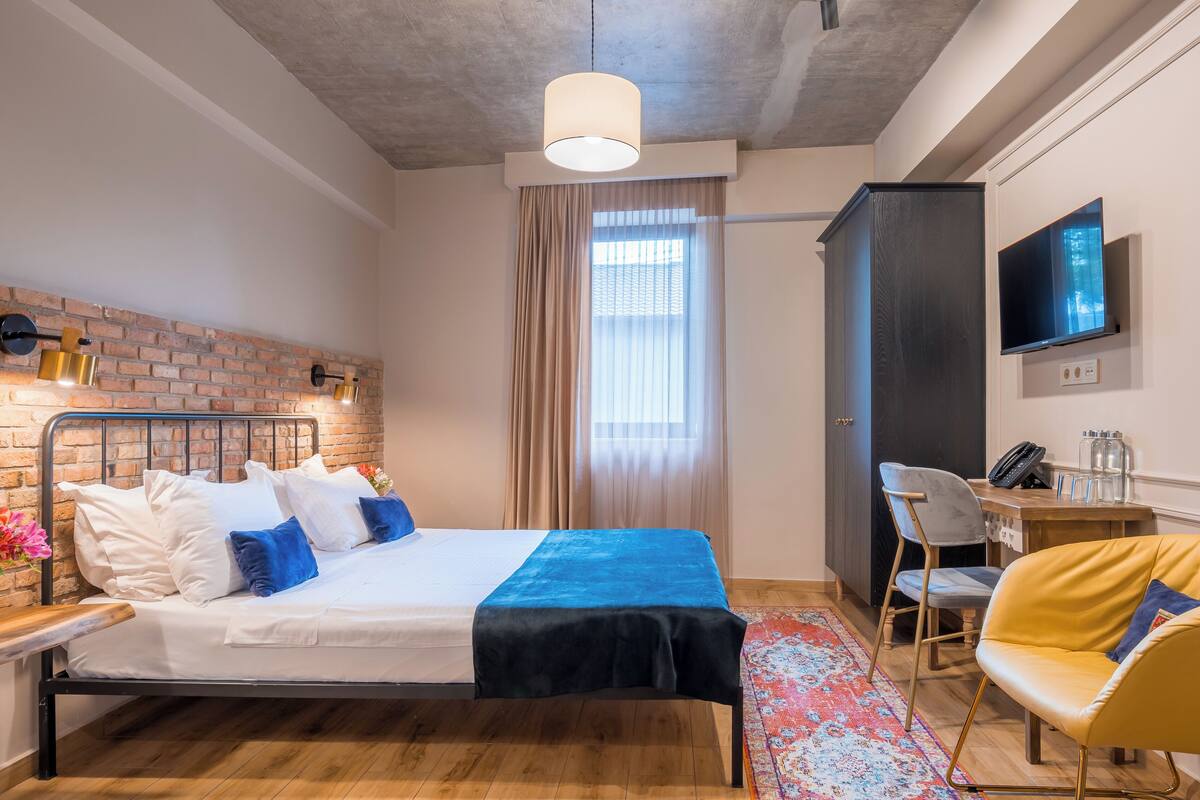 Een moderne hotelkamer met een bed, een bureau met stoel, een televisie en een bakstenen muur.