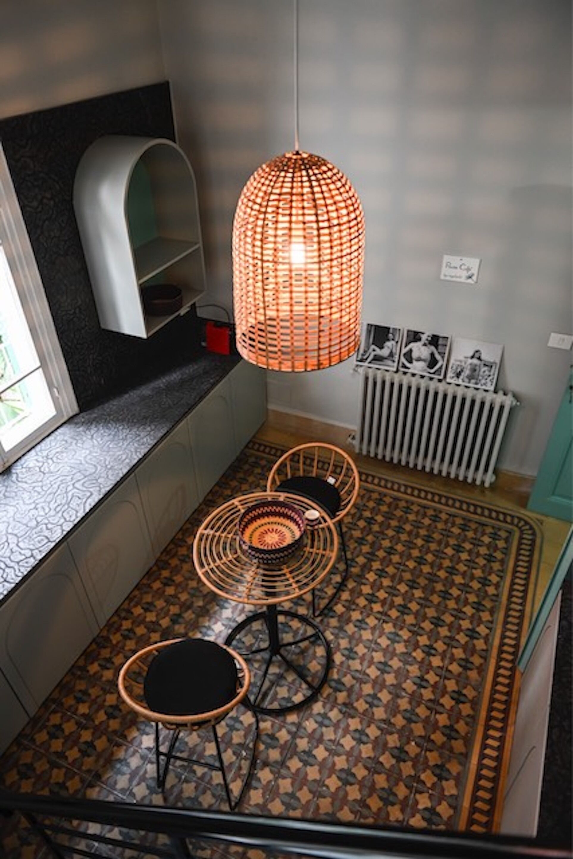 Una cocina compacta con una lámpara colgante naranja, estante empotrado, radiador y suelo estampado.