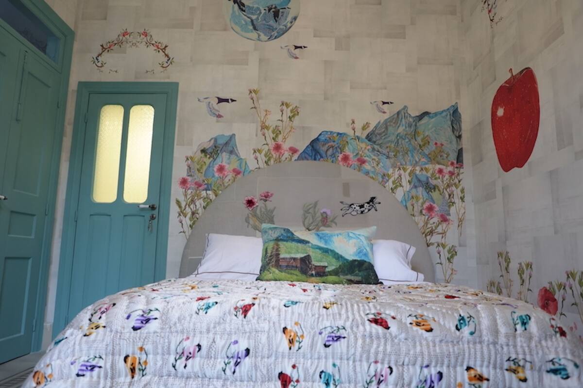 A bedroom with a bed, floral wall art, a blue door, and a red apple on the wall.
