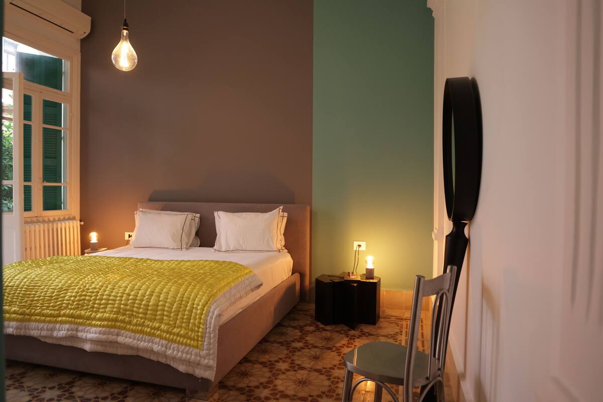 A bedroom with a bed, bedside lamps, a chair, and a wall-mounted speaker.