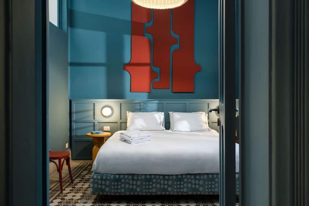 A modern hotel room with a large bed, a round wall clock, and a unique red and blue wall design.