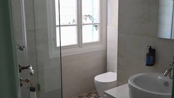 A bathroom with a glass shower enclosure, a toilet, a sink, and a window providing natural light.